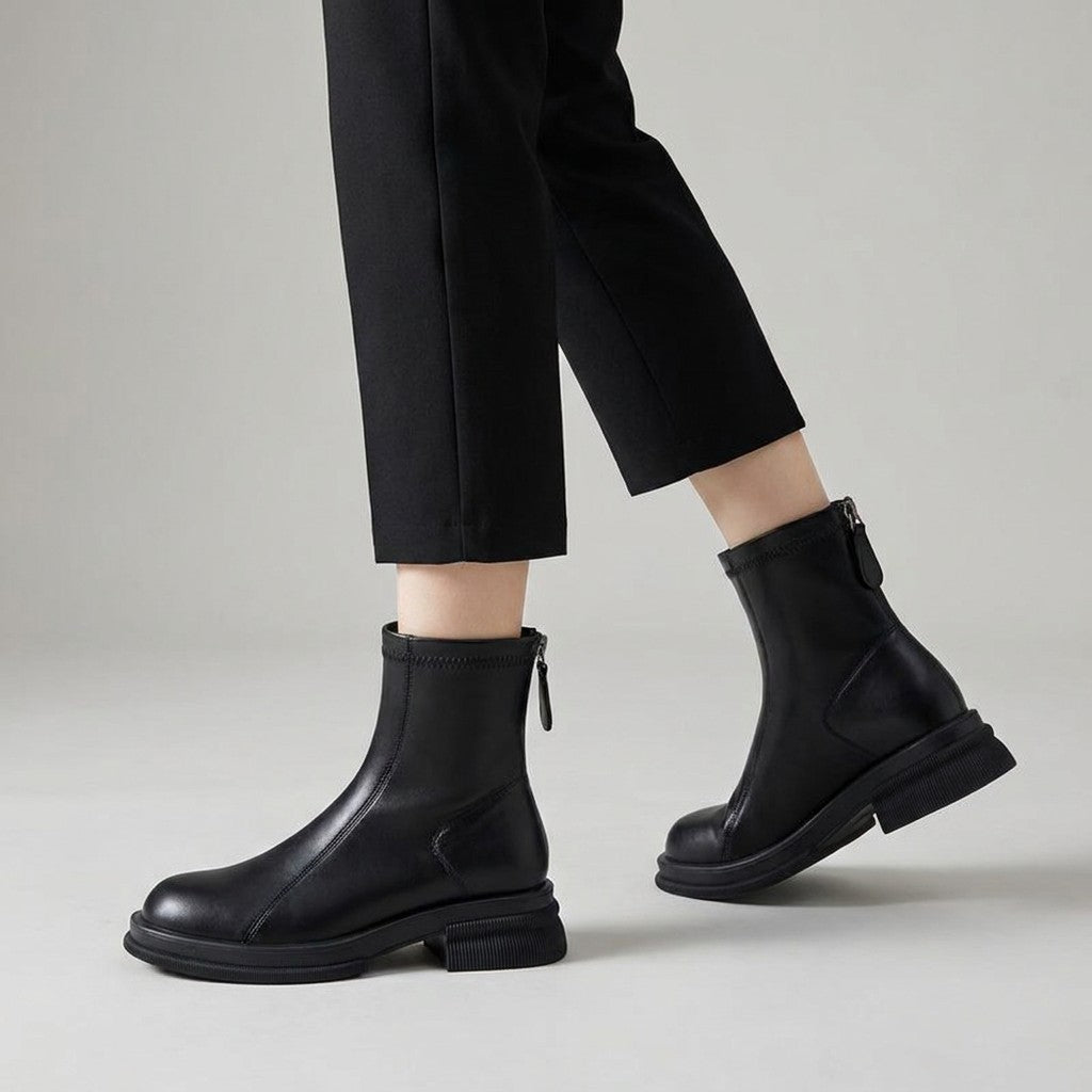 Black Liesel ankle boots worn mid-stride, showing the back zip pull and block heel
