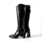 Pair of black Mirela leather knee high boots with flared block heels and lug soles on white