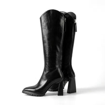 Pair of black Mirela leather knee high boots with flared block heels and lug soles on white