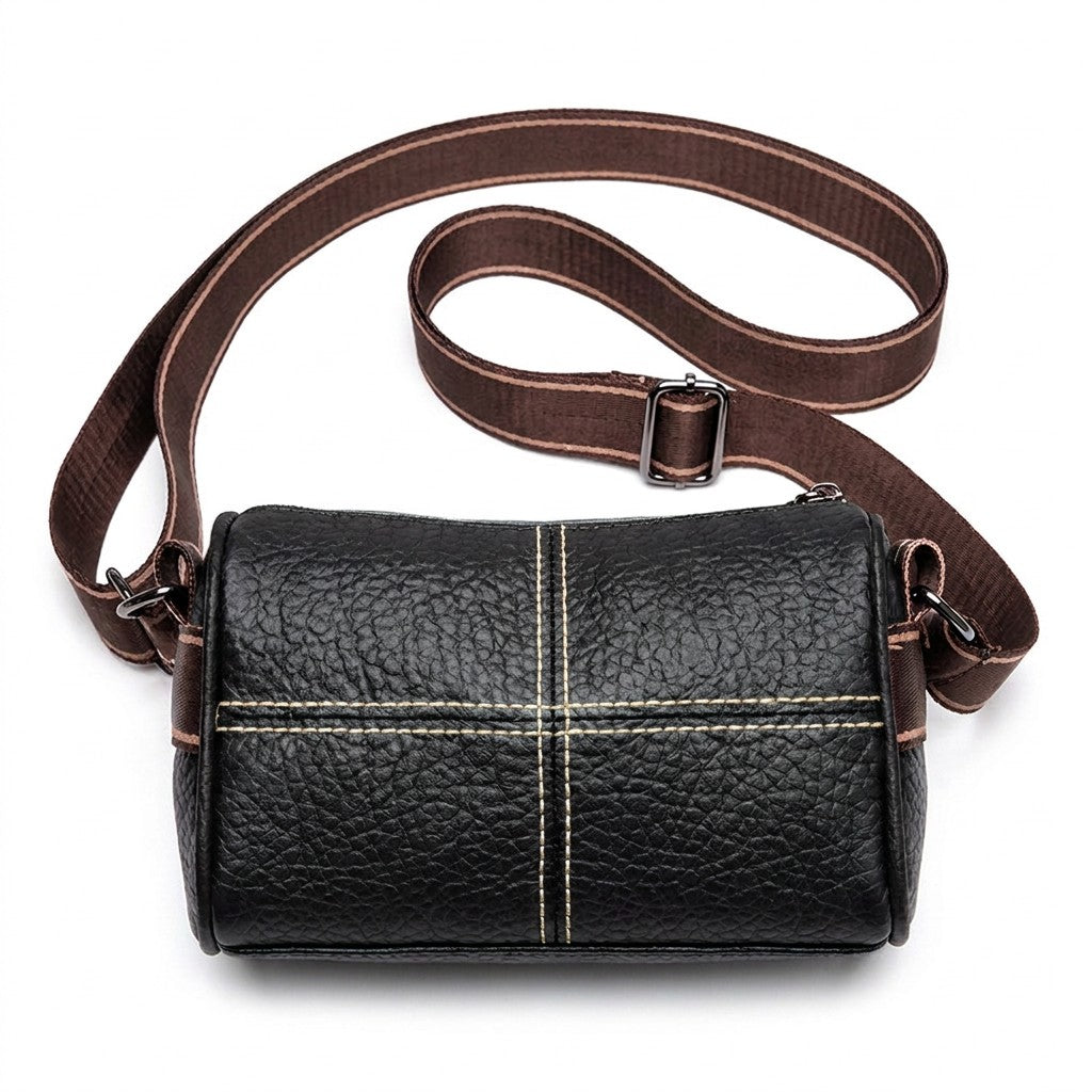 Front view of the Bellamy black pebbled leather barrel crossbody bag with cream cross stitching and wide woven strap