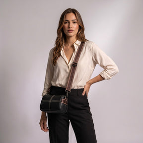 Model wearing the black Bellamy crossbody bag at her hip with an ivory silk blouse and black trousers