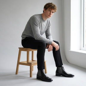 Model seated on a wooden stool wearing black Jasper Chelsea boots