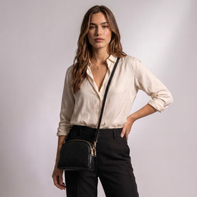 Model wearing the black Isaure half-moon bag crossbody with an ivory silk blouse and black trousers