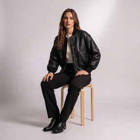 Model seated on a wooden stool in the Aurelia cropped leather bomber and black trousers