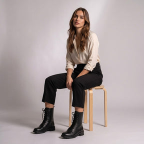 Model seated on a wooden stool wearing black Lysandra combat boots