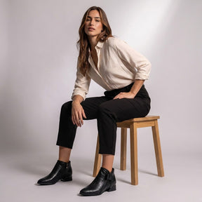 Model seated on a wooden stool wearing black Tamsin croc-embossed ankle boots