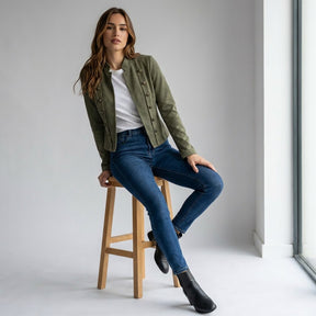 Model seated on a wooden stool in the army green Elodie jacket and jeans