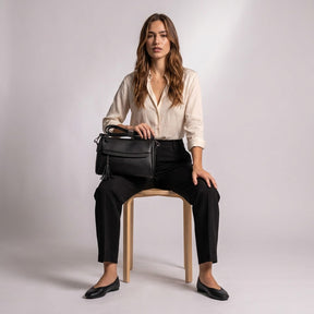Model seated on a wooden stool with the black Odalys leather bag resting on her lap