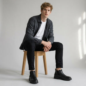 Model seated on a wooden stool wearing black Henrik boots with black jeans