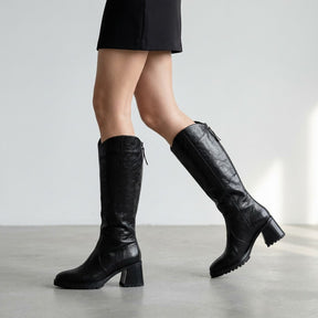 Black Mirela boots mid-stride, side view of the crinkled leather shaft and treaded sole