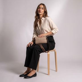 Model seated on a wooden stool with the beige Bellamy leather bag on her lap