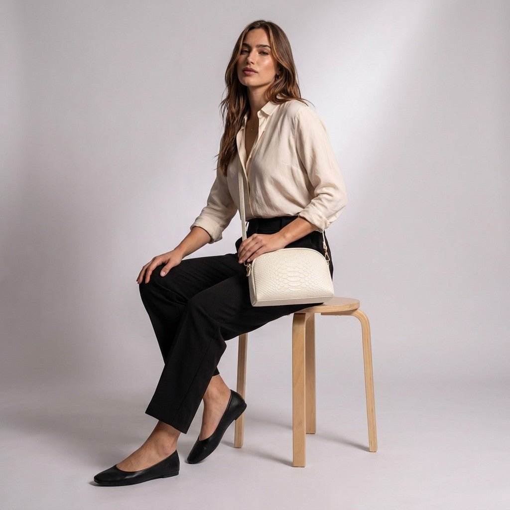 Model seated on a wooden stool wearing the cream Isaure crossbody bag