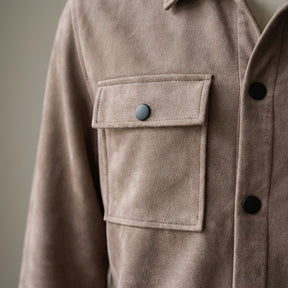 Close-up of the Dorian chest pocket flap, black snap and topstitching in taupe suede